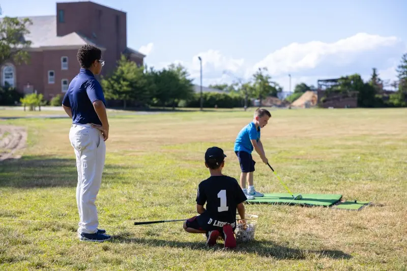 An instructor watches a junior’s swing on the range