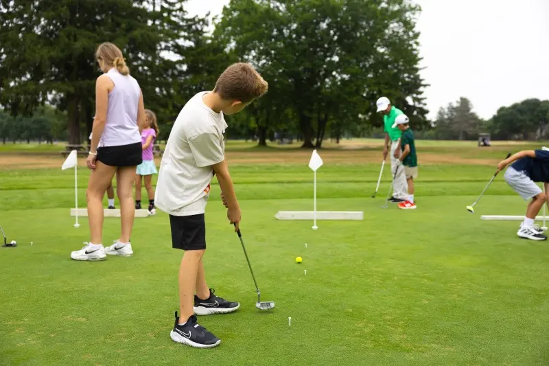 A junior putts while coaches look on