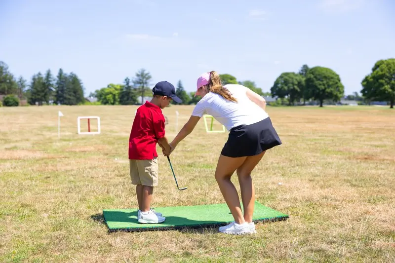 A coach sets a junior’s grip on a hitting mat