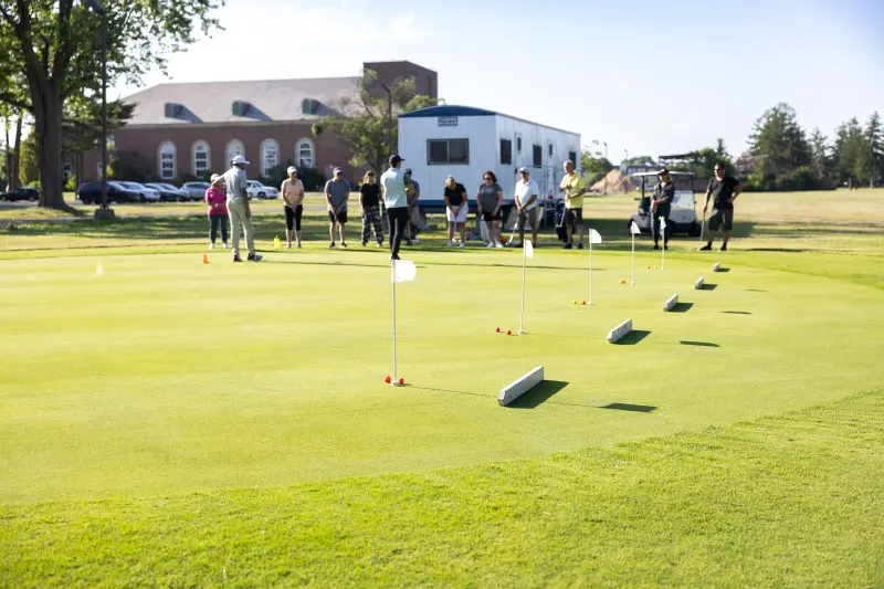 Adult students practicing chips on the short-game green