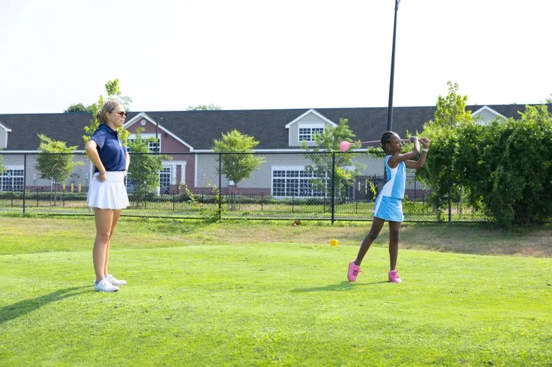 A junior finishes her swing on the practice green