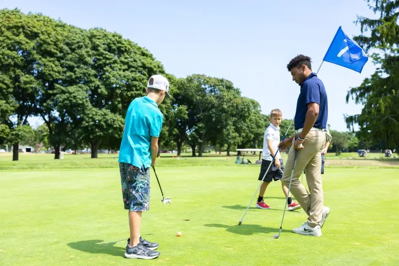 A junior hits a shot as a coach looks on