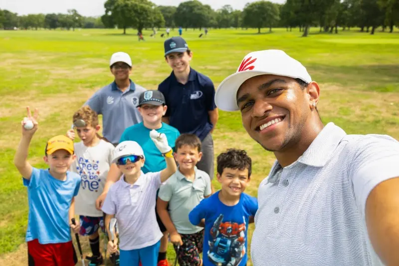 A coach takes a selfie with a group of smiling junior golfers