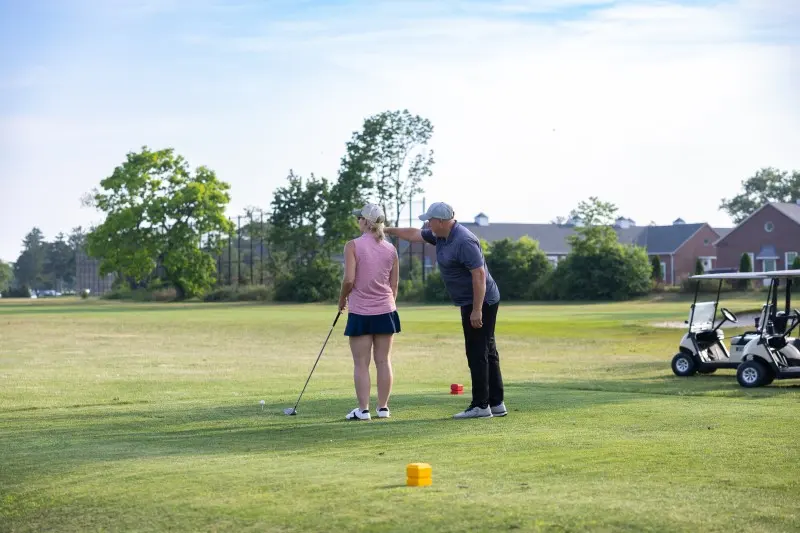 An instructor coaches a golfer on the practice green