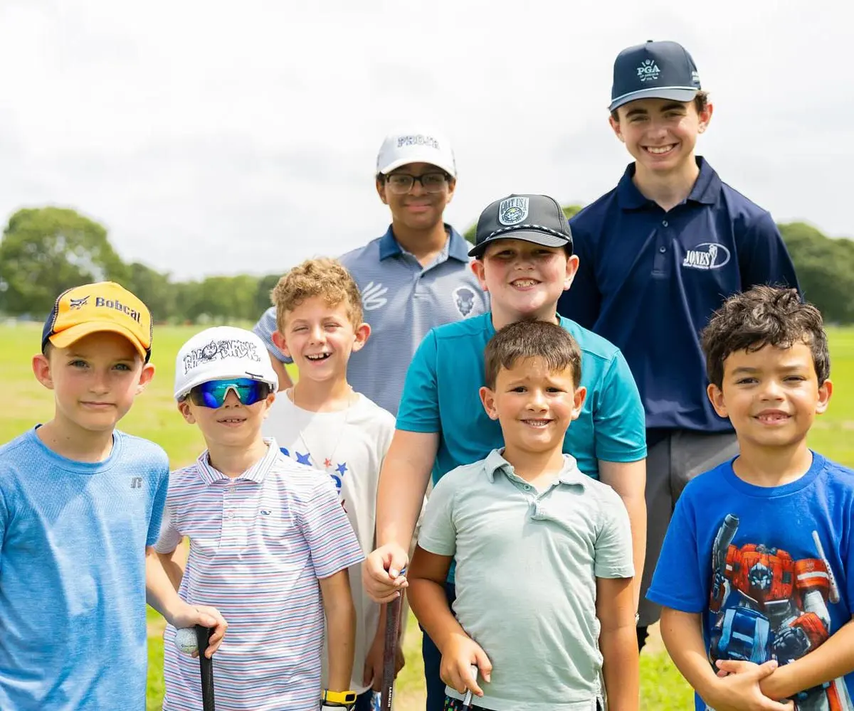 Junior golfers in caps and polos crowd together for a photo on the range