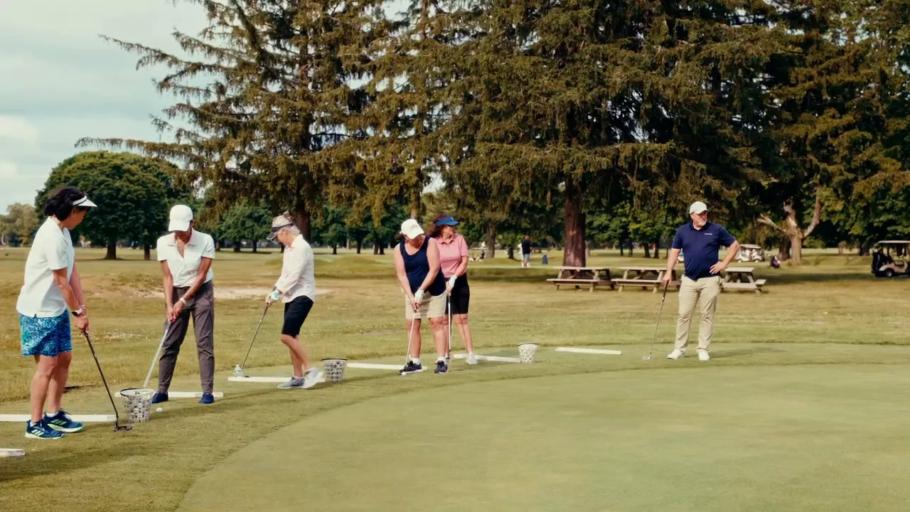Adult students practice on the green while their instructor watches