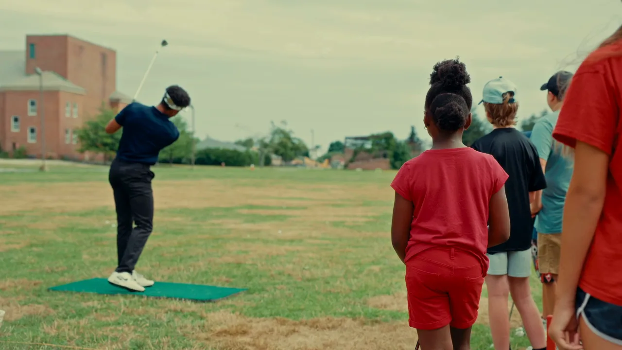 A coach demonstrates a full swing while juniors watch from behind